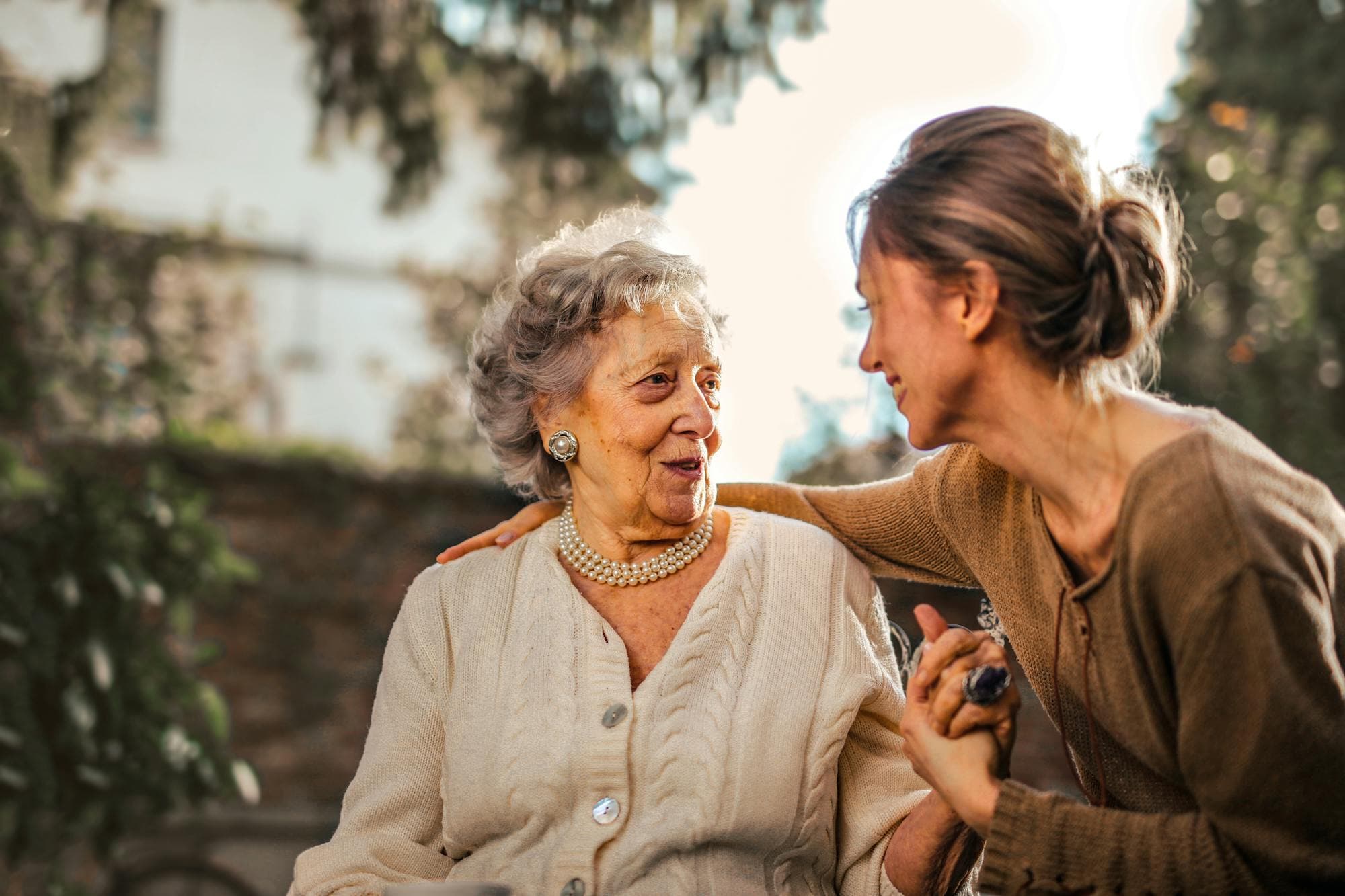 An adult daughter and her senior mother sharing a joyful moment together in a sunlit garden.